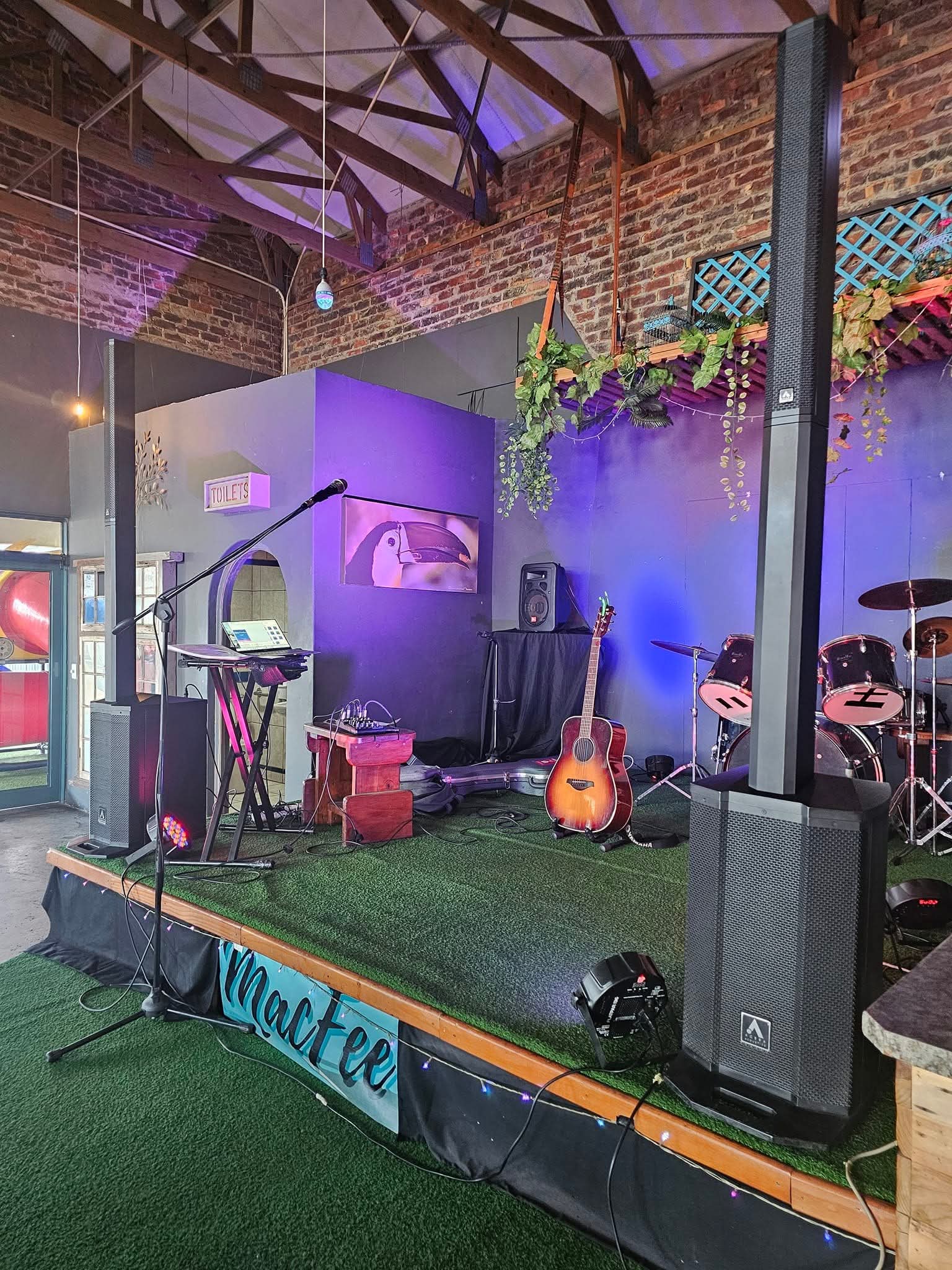 Speaker columns and guitar setup on a brick-walled indoor stage