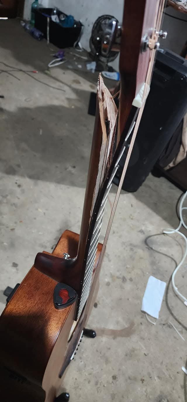 Side view of a damaged guitar neck or headstock area before repair